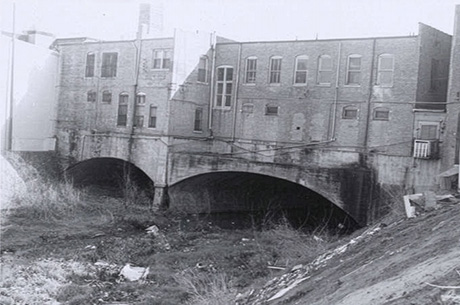 A brick building constructed over arched concrete bridge supports on Marine Creek